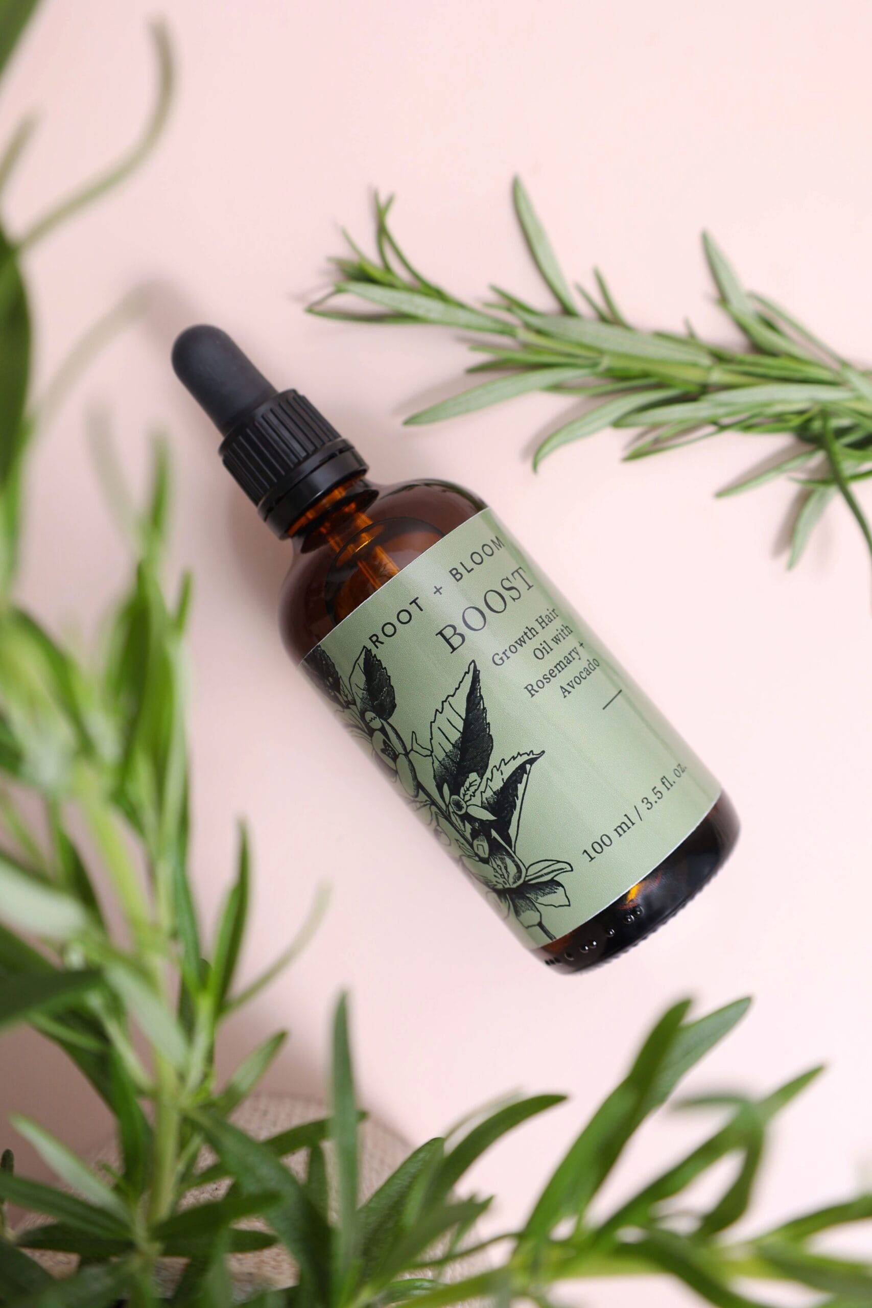 Rosemary hair oil in an amber dropper bottle surrounded by fresh rosemary sprigs